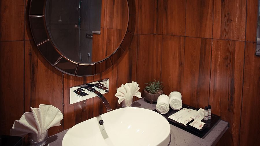 Deluxe King Room washroom with a round mirror and wooden paneling at Clarks Inn Suites Jaipur, Ajmer Road
